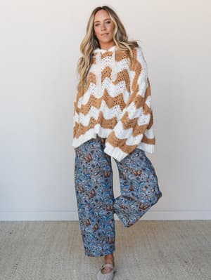A relaxed, boho-leaning two-piece outfit pairing an oversized chevron crochet sweater in caramel and cream with wide-leg butterfly print pants in dusty blue — the kind of mix-and-match energy that looks effortless but was definitely thought about.