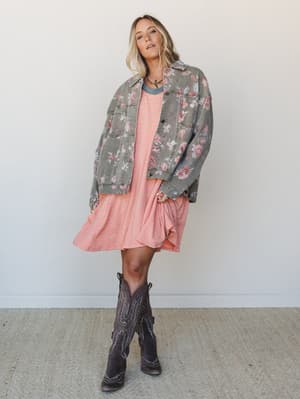A relaxed, mix-print outfit pairing a striped mini dress with an oversized floral denim jacket and dark cowboy boots — the kind of effortless combo that looks like it came together on purpose but feels like a happy accident.