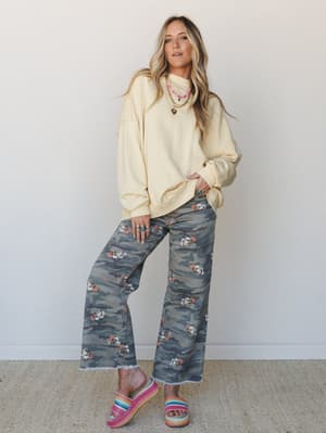 An oversized butter-yellow sweatshirt meets camo-floral wide-leg jeans and rainbow platform slides — the kind of outfit that looks effortless but definitely took a second thought, in the best way.