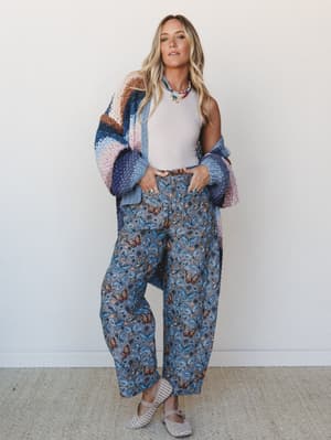 A relaxed, expressive outfit pairing wide-leg butterfly-print pants with an oversized chunky color-block crochet cardigan and a simple white tank — the kind of look that feels effortless but is clearly very much on purpose.