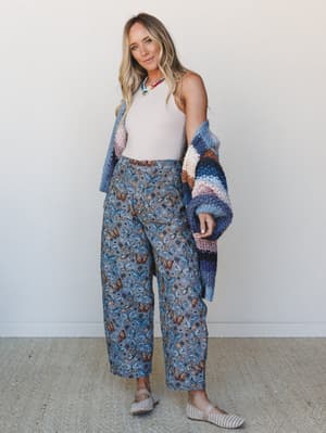 A relaxed full-body shot of a model in butterfly-print wide-leg pants and a sleeveless white tank, layered under a chunky striped knit cardigan — the kind of outfit that somehow looks both effortless and thought-through.