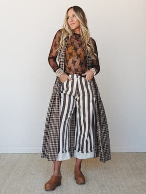A layered three-piece look built around chocolate brown tones — sheer floral lace top, gingham duster, and wide-leg striped trousers — styled with stacked bracelets and wood-soled clogs for a mix-print moment that feels intentional, not accidental.
