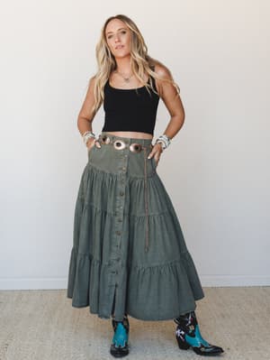 A tiered olive denim maxi skirt styled with a black crop tank, turquoise embroidered cowboy boots, and a copper concho belt — the kind of outfit that looks like it was thrown together effortlessly but absolutely wasn't.