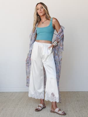 A relaxed, sun-kissed look built around wide-leg satin pants with lace hem trim, styled with a cropped ribbed tank and a flowing floral kimono draped off the shoulder — the kind of outfit that works just as well for a morning farmers market as it doe