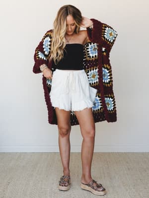 A granny square crochet cardigan in deep wine anchors the look — layered over a black tube top and raw-hem fleece shorts, it's the kind of outfit that feels intentional without trying too hard.