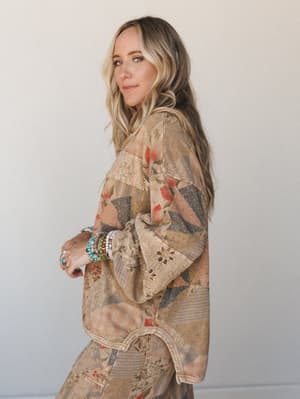 A relaxed, sun-warmed look — model shot in profile wearing a mixed patchwork floral top with wide balloon sleeves and matching floral pants, layered with colorful beaded bracelets and rings for that perfectly collected boho feel.
