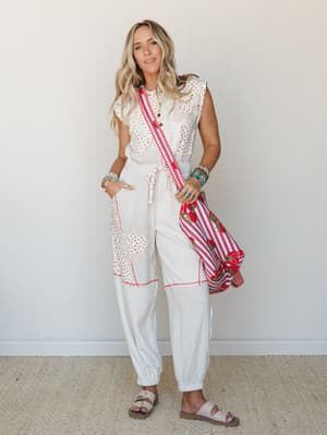 A breezy, patchwork-detailed white two-piece set styled with a strawberry-print striped tote, stacked turquoise bracelets, and white sandals — the kind of outfit that feels equally at home at a farmers market or a backyard brunch.