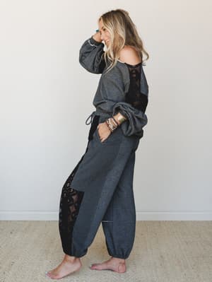 A smiling model shot in profile wearing a matching charcoal sweatshirt-and-jogger set with black lace panel insets — the kind of cozy outfit that makes staying in feel intentional.