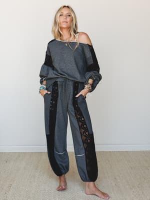 A charcoal and black two-piece set with lace panel detailing worn casually off-the-shoulder, styled with layered turquoise and gold jewelry for a relaxed boho feel.