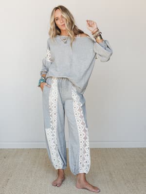 A relaxed two-piece matching set in heather grey with wide crochet lace side panels — styled with stacked turquoise and gold bracelets and a delicate necklace, giving off that effortless 'stayed home but make it intentional' energy.