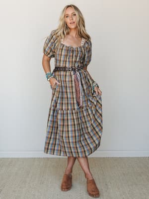 A plaid midi dress styled with a leather belt, scarf tie, and stacked turquoise bracelets — earthy, expressive, and the kind of outfit that makes a farmers market feel like a destination.