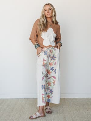 A relaxed two-piece set pairing a mocha cropped sweatshirt with a large white floral appliqué against wide-leg floral print pants — the kind of outfit that looks effortless but clearly thought about.