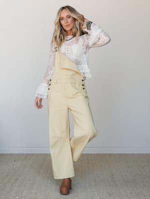 A relaxed, sun-washed look pairing wide-leg butter yellow overalls with a sheer lace long-sleeve top — the kind of outfit that feels effortless but clearly wasn't an accident.