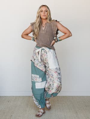 A model styled in a relaxed patchwork harem pant and mocha ruffle-sleeve top, layered with beaded bracelets and sandals — the kind of outfit that looks effortless but clearly had a whole vibe going on.
