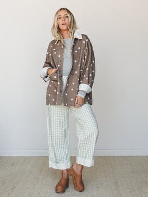 A layered, pattern-mixed outfit that feels like a Saturday with nowhere to be — an oversized polka dot jacket over a grey tee, sage gingham wide-leg pants with rolled cuffs, and brown studded clogs that tie the whole earthy moment together.
