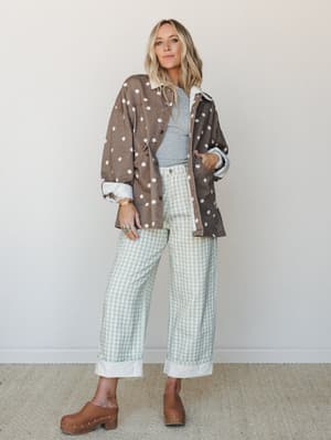 A relaxed, pattern-mixed outfit pairing an oversized polka dot shacket with sage gingham wide-leg jeans and a grey tee — the kind of effortlessly collected look that makes you want to go thrifting and then grab coffee.
