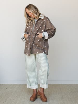 A relaxed, pattern-mixed outfit — an oversized polka dot shacket layered over a light tee and sage gingham wide-leg pants with cuffed hems, finished with brown wood-studded clogs — the kind of look that feels effortless and a little unexpected in the
