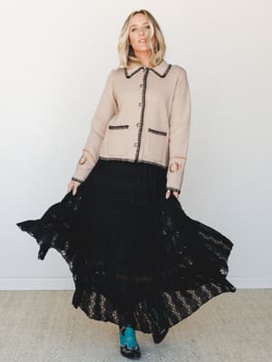 A flowing black lace maxi skirt pairs with a sand-colored cropped cardigan trimmed in black whipstitch and horseshoe embroidery — the kind of outfit that feels equally at home at a fall concert or a candlelit dinner, especially with those teal cowboy