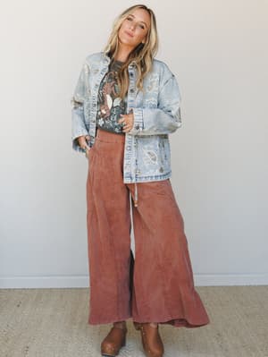 A relaxed, lived-in outfit layered with intention — wide-leg rust pants, an embellished denim jacket, and a graphic tee come together in that effortless way that looks like you just threw it on and somehow nailed it.