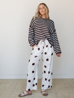 A mixed-print moment that somehow just works — an oversized brown and sky blue striped knit sweater paired with cream wide-leg pants in a bold polka dot print, grounded with neutral slide sandals for an effortlessly relaxed finish.