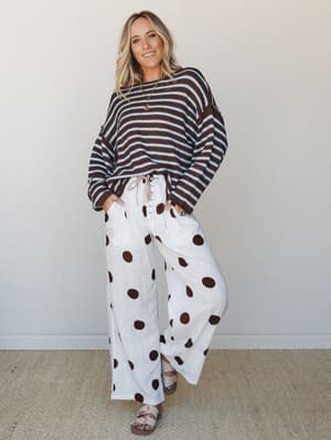 A mixed-print moment done right — striped brown and sky blue knit sweater paired with oversized polka dot wide-leg pants in cream and chocolate, styled with sandals for an effortlessly playful, lived-in look.