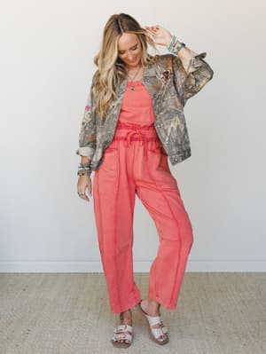 A coral two-piece set — relaxed tank and wide-leg jogger pants with a drawstring waist — layered under an open camo jacket with patches, styled with beaded bracelets, a pendant necklace, and white buckle sandals for an effortless boho-western feel.