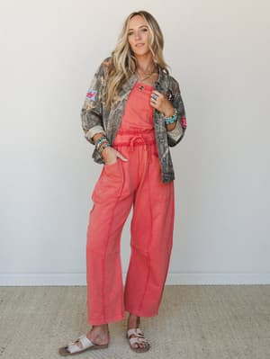 A relaxed, color-forward two-piece set in washed coral-orange is styled under an open camo shacket with iron-on patches — the kind of outfit that feels effortless but clearly thought through, finished with turquoise stacked bracelets and white slide