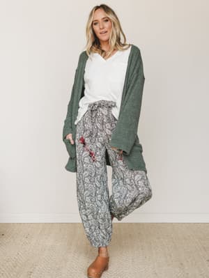 A relaxed, layered look built around wide-leg paisley pants, a chunky forest green cardigan, and a white v-neck tee — the kind of outfit that makes staying in feel just as intentional as going out.