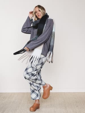 A relaxed fall outfit with easy attitude — oversized gray sweater, plaid wide-leg pants, and a fringed blanket scarf worn loosely, finished with caramel clogs and a stack of turquoise jewelry.