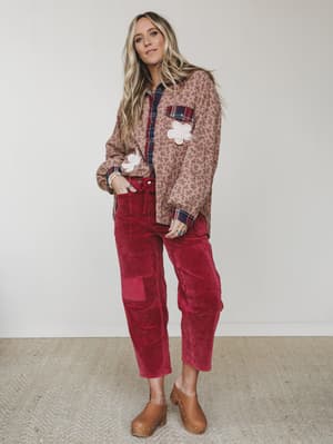 A layered fall outfit with a mixed-print floral shacket over a plaid button-down, styled with deep crimson corduroy cargo pants and tan wooden clogs — the kind of put-together-but-relaxed look that makes autumn dressing feel easy.