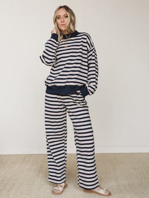 A matching navy stripe two-piece set — oversized sweatshirt and wide-leg pants — styled with layered gold necklaces and white sandals for that effortlessly put-together, cozy-but-going-somewhere energy.