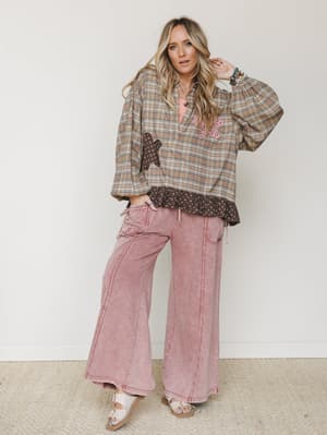 A relaxed, lived-in outfit pairing an oversized plaid top with floral patchwork appliqué and a ruffled hem over wide-leg mineral-washed pants in dusty rose — effortlessly boho and the kind of look that just works.
