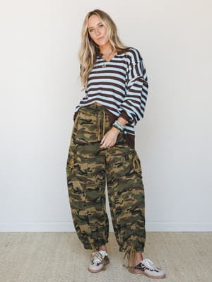 A relaxed, mix-print outfit pairing wide-leg camo cargo pants with a striped knit sweater — the kind of effortless combo that looks like you meant to do it, styled with leopard sneakers and stacked turquoise bracelets.