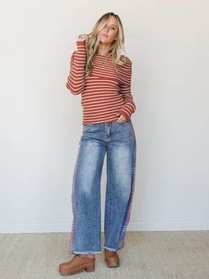 A rust-striped ribbed sweater paired with wide-leg jeans featuring plaid side panels and frayed hems — the kind of outfit that feels like fall weekends done exactly right.