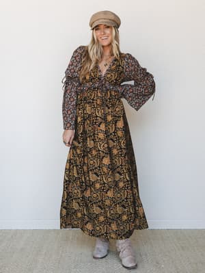 A mixed floral print maxi dress with dramatic puff sleeves and a tiered skirt, styled with a tan baker boy cap and slouchy suede boots — the kind of autumn outfit that makes a grocery run feel like a countryside adventure.