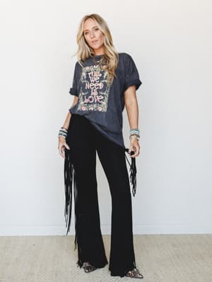 A relaxed, rock-meets-boho full look — an oversized vintage-style graphic tee tucked loosely into wide-leg black fringe pants, styled with stacked bracelets and leopard pointed-toe flats for a free-spirited, concert-ready vibe.