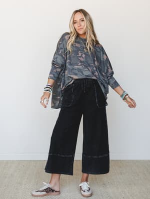 A relaxed, lived-in outfit pairing an oversized camo long-sleeve top with wide-leg black cropped pants — the kind of effortless combo that looks like you tried just the right amount.