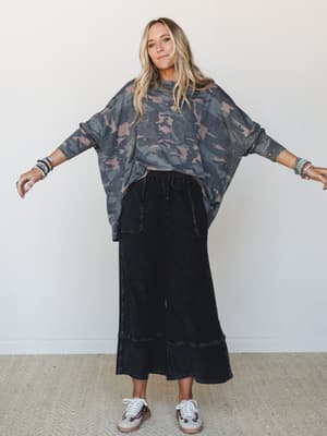 An oversized camo dolman top paired with wide-leg black crop pants and leopard-print sneakers — the kind of effortless, thrown-together outfit that somehow looks completely intentional.