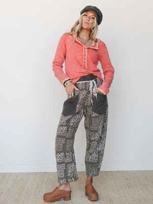A relaxed, lived-in outfit pairing a washed coral henley pullover with wide-leg bandana patchwork pants, clogs, and a baker boy cap — the kind of put-together-without-trying look that feels genuinely personal.