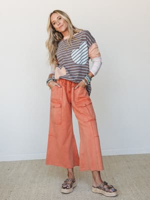 A fun, color-mixed outfit pairing a striped long-sleeve top with a heart graphic pocket and contrast sleeves against wide-leg cropped coral cargo pants — playful and relaxed with a boho-casual energy.