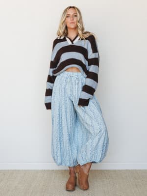 A relaxed, mix-print two-piece moment — bold brown and blue stripe cropped sweater paired with flowy floral wide-leg pants in the same soft blue, grounded by tan studded clogs for a look that's effortlessly put-together without trying too hard.