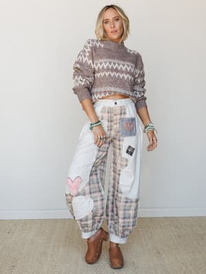 A relaxed, expressive outfit pairing a cropped Fair Isle knit sweater with wide-leg patchwork pants covered in heart appliqués — the kind of look that feels like a warm hug and a personality statement at the same time.