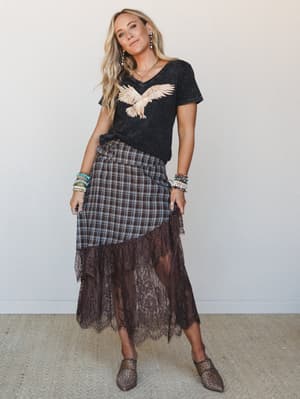 A boho-meets-rocker outfit built around a washed graphic tee and a plaid wrap skirt with a dramatic lace hem — the kind of look that feels effortlessly pulled together and slightly untamed, finished with leopard mules and stacked bracelets.