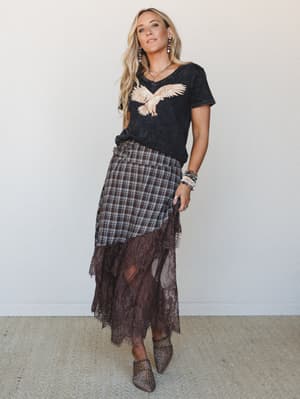 A layered boho-rock outfit — acid wash graphic tee tucked into a plaid midi skirt with a sheer lace hem layer — styled with leopard mules and stacked jewelry for that effortless, slightly-edgy free spirit feel.