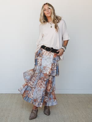 A flowy tiered maxi skirt in dusty blue and rust floral print is paired with an oversized cream tee, studded belt, and leopard mules — the kind of put-together-but-effortless outfit she'd wear to brunch and not want to take off.
