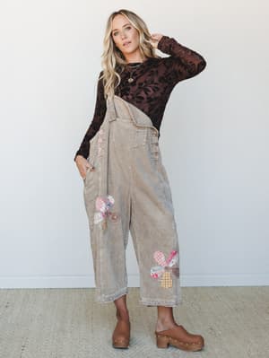A wide-leg corduroy overall styled over a dark floral mesh long-sleeve, finished with clogs and layered necklaces — the kind of outfit that feels like it was put together effortlessly but absolutely wasn't.
