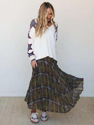 A flowy plaid maxi skirt in olive and brown paired with a cream knit sweater featuring star graphics on the sleeves — the kind of mix-and-match outfit that looks effortless but was definitely thought about.