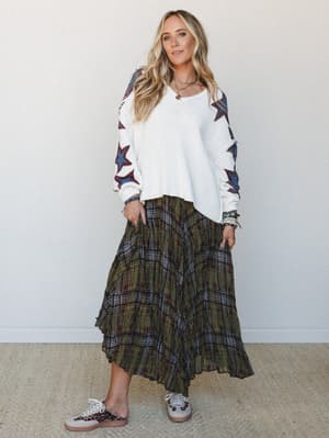 A relaxed, pattern-mixed outfit pairing a cream knit sweater with bold star-print sleeves against a flowy olive plaid maxi skirt — the kind of effortless combo that looks like you meant to do it.