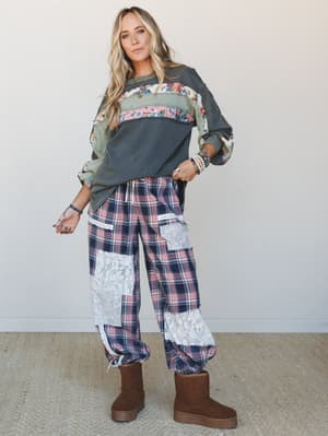 A relaxed full-body model shot of a patchwork-loving outfit pairing — an oversized floral-panel sweatshirt with a plaid and lace patchwork wide-leg pants, finished with platform sherpa boots and layered bracelet stacks that feel collected, not coordi
