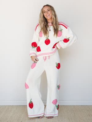 A matching cream knit sweater and wide-leg pant set covered in playful embroidered strawberries in red and pink — the kind of outfit that makes you smile before you even put it on.
